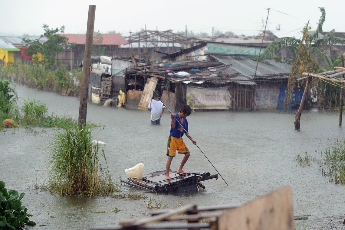 Ein Junge stakst durch einen überschwemmten Slum